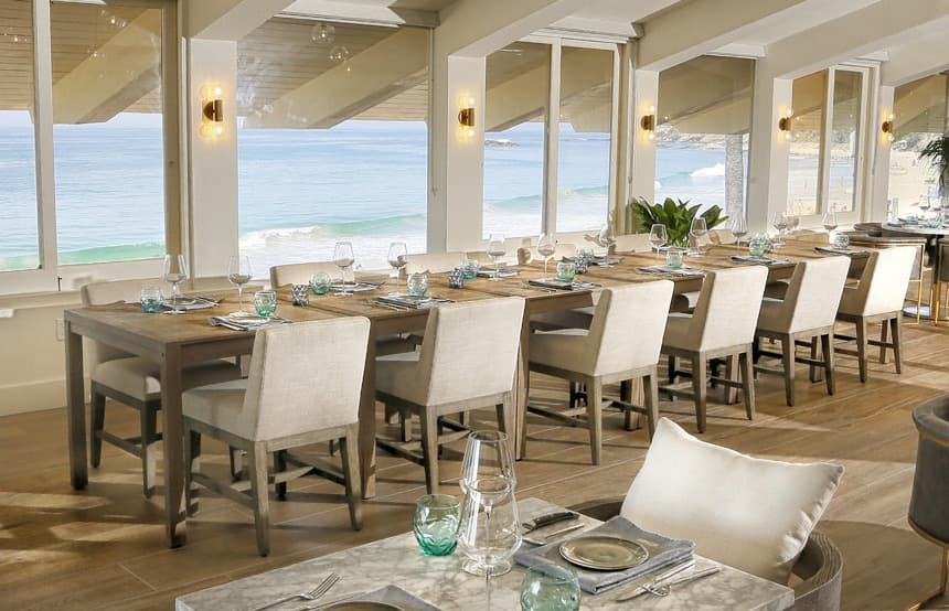 An oceanfront dining room, with a long communal table set toward the water.